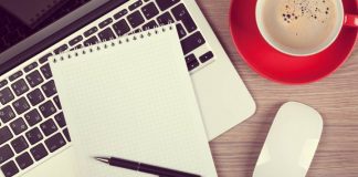 Blank notepad over laptop and coffee cup on office wooden table